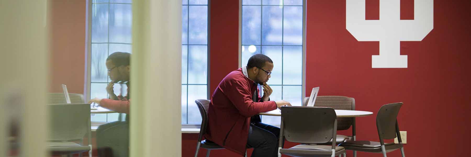 A student works on a computer in front of an IU trident.