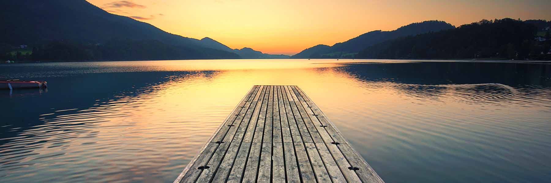 A lonely wooden pier out into a still lake at sunset