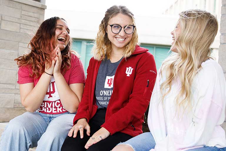 Three students on a bench in front of Briscoe, laughing.