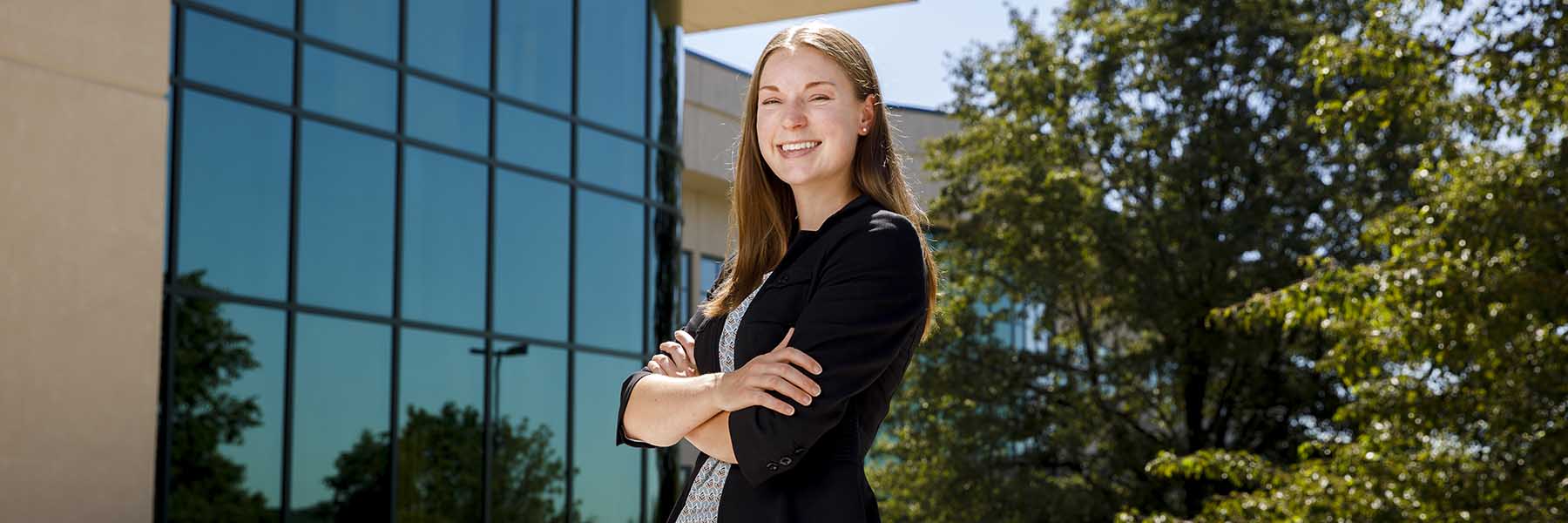 Smiling woman in professional attire smiles in a business park setting. 