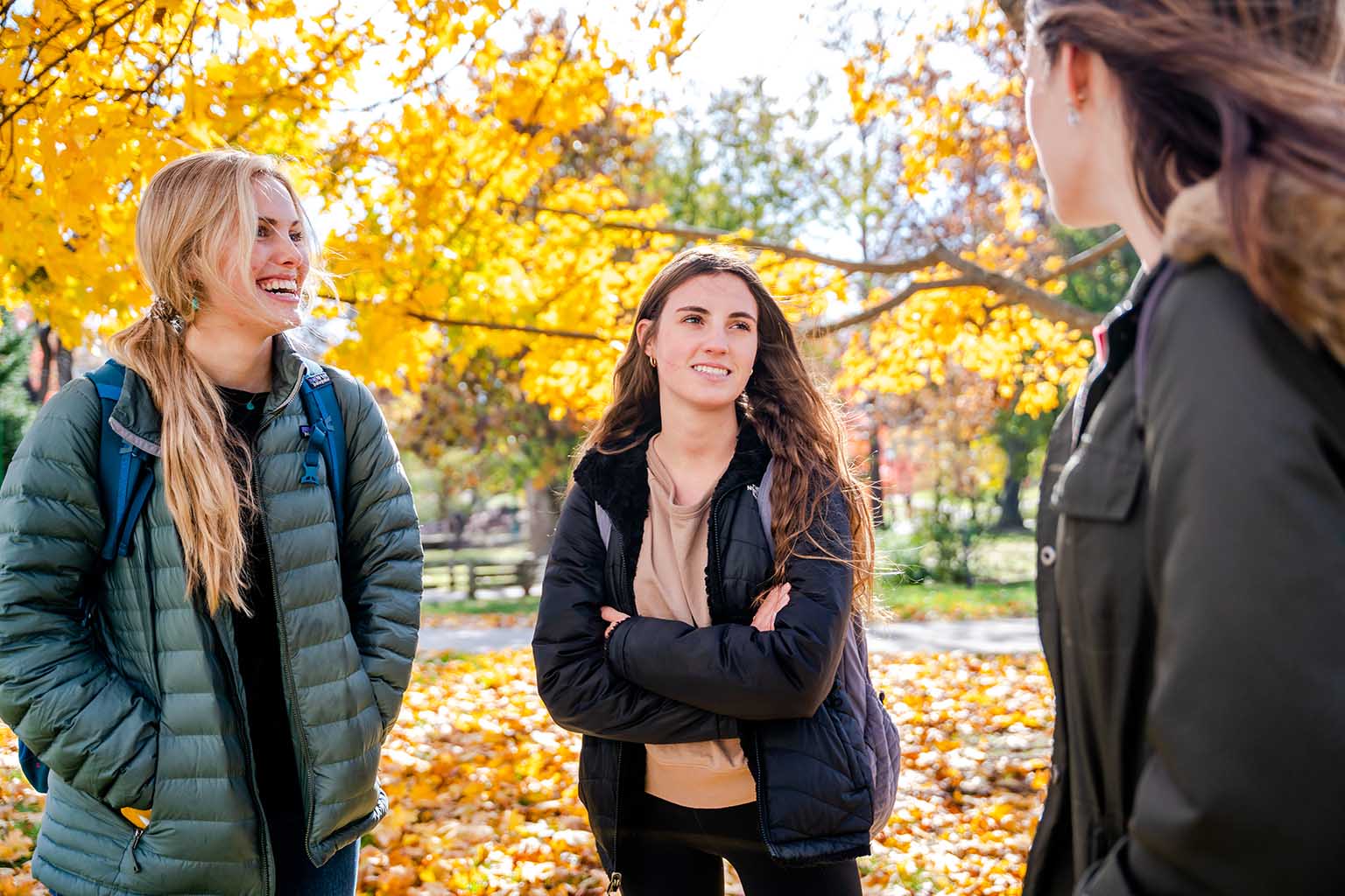 Three women students talk outside in the fall weather